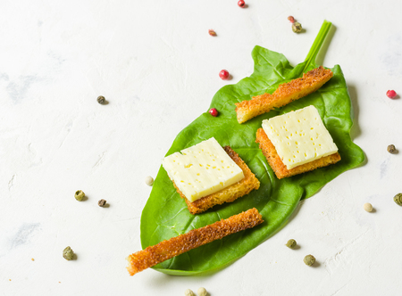 Croutons with cheese lying on a green sheet of spinach. White stone background. Place for the text.の写真素材