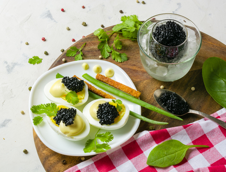 Appetizer of eggs, white sauce and black caviar. Layout on a wooden background with spices and herbs. View from above.の写真素材