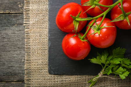 Branch with five ripe red tomatoes. Drops of water on ripe fruits. Green leaves and trunk. Copy space.の写真素材