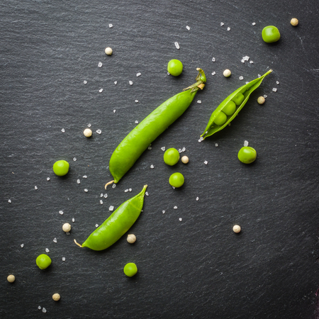 Open and closed Pellets of green peas on a black stone background. Fresh fruits. Harvesting. View from above.の写真素材