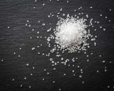 A bunch of white salt crystals on a black stone background. Seasoning for eating. Scattered over the surface. Copy space.の写真素材