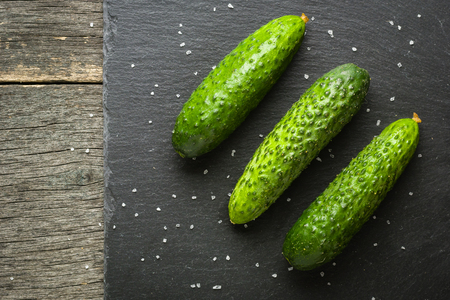 A few fresh green cucumbers lying side by side on a black stone background. A minimalistic photograph. Copy space.の写真素材