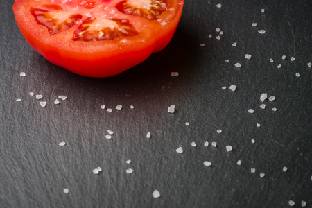 Cut tomato red with seeds and patterns. View from above. Black stone slate background. Copy space.の写真素材