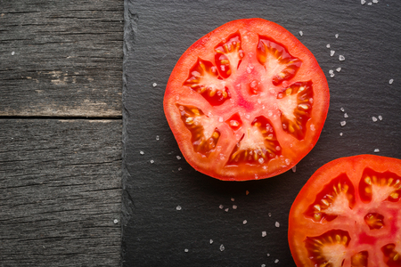 Cut tomato red with seeds and patterns. View from above. Black stone slate background. Copy space.の写真素材