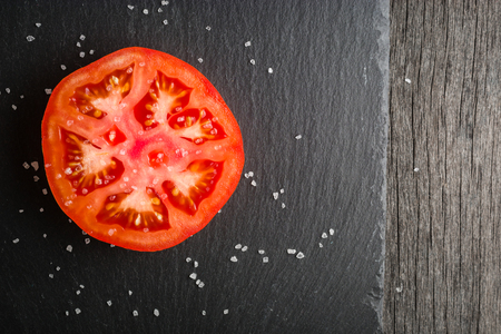 Cut tomato red with seeds and patterns. View from above. Black stone slate background. Copy space.の写真素材