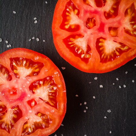 Cut tomato red with seeds and patterns. View from above. Black stone slate background. Copy space.の写真素材