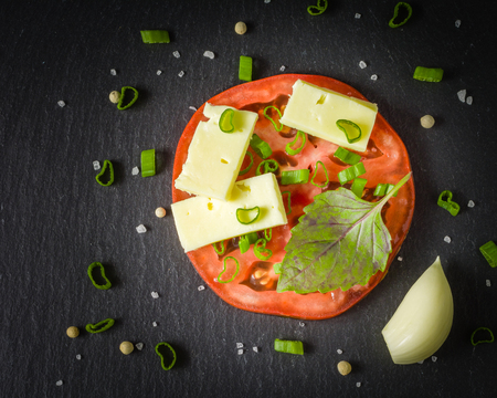 Half a tomato with cheese and a green onion on it. Pieces of mozzarella and seasoning. Copy space.の写真素材