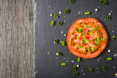 Cut tomato red with seeds and patterns. View from above. Black stone slate background. Copy space.の写真素材
