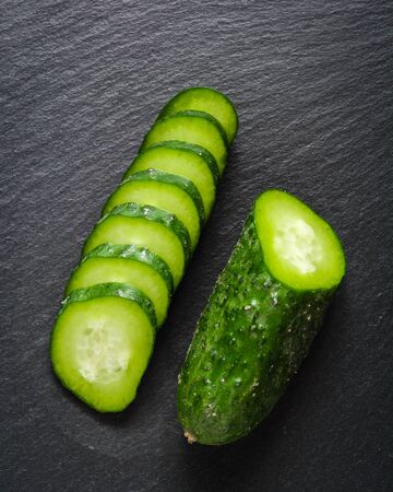 Fresh green sliced cucumber on a black stone background. Copy space.の写真素材