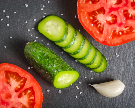 Fresh green sliced cucumber and tomato on a black stone background.Copy space.の写真素材