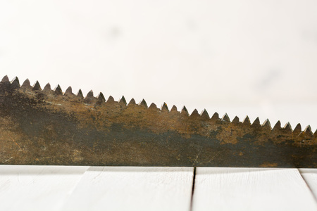 Large teeth of an old saw on wood. Sharp and uneven edges. Rusted surface. Light stone background. Copy space.の写真素材