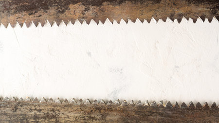 Large teeth of an old saw on wood. Sharp and uneven edges. Rusted surface. Light stone background. Copy space.の写真素材
