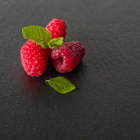 Ripe juicy raspberries on a dark background. Fresh green mint leaves. View from above.の写真素材