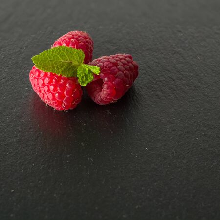 Ripe juicy raspberries on a dark background. Fresh green mint leaves. View from above.の写真素材