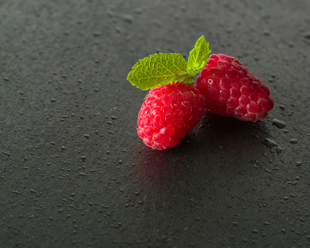 Ripe juicy raspberries on a dark background. Fresh green mint leaves. View from above.の写真素材