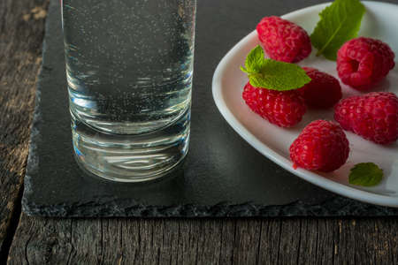 Ripe juicy raspberries on a plate on dark background. Fresh green mint leaves. View from above.の写真素材