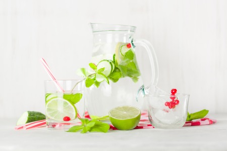 Detox water in a glass jug and a glass. Berries and lime, red and green. Fresh mint leaves. Bright white background.の写真素材