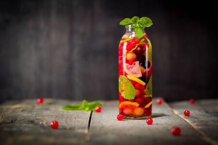 Bottle with detox water, berries and citrus inside. Dark background and old wooden table surface. Copy space.の写真素材