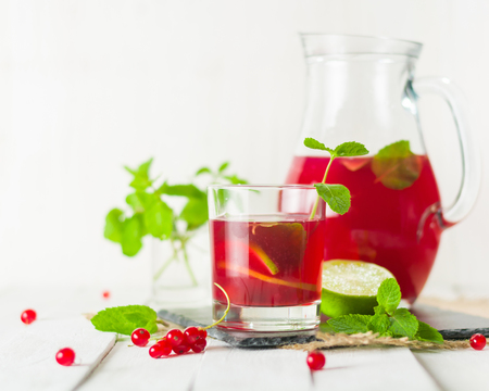 Compote in a glass jug and a glass. Berries and lime, red and green. Fresh mint leaves. Bright white background.の写真素材