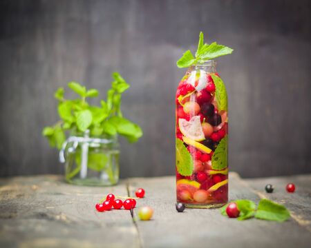 Bottle with detox water, berries and citrus inside. Dark background and old wooden table surface. Copy space.の写真素材