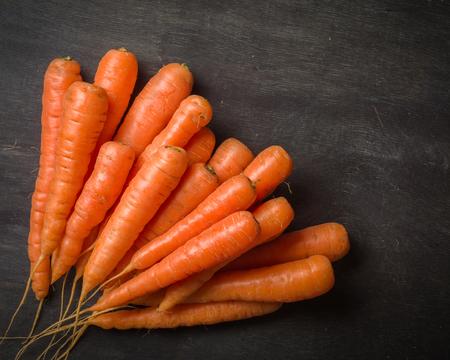 Carrots of various sizes stacked in a pile on a black wooden background. Washed and ready to eat.の写真素材