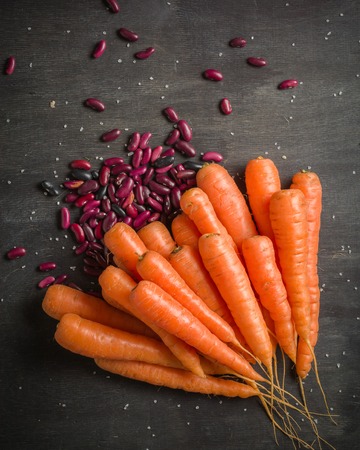Carrots of various sizes stacked in a pile on a black wooden background. Washed and ready to eat.の写真素材