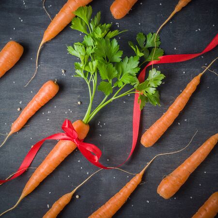 Carrots with a gift red ribbon, green tops on a black background. View from above.の写真素材
