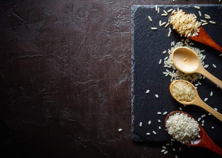Rice of different varieties in wooden spoons on a dark background. Slate stone background. Plenty of room for text. Copy space.の写真素材