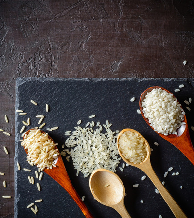 Rice of different varieties in wooden spoons on a dark background. Slate stone background. Plenty of room for text.の写真素材