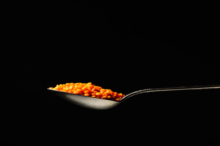 Metal silver spoon with the product in it. Orange lentils or beans. Large side view. Black dark background. Plenty of room for text.の写真素材