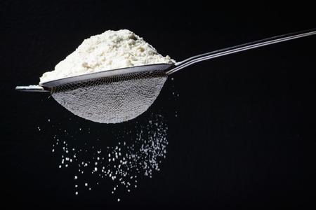 Flour is poured into a sieve, which sifts it. Dark and black background. Flour movement.の写真素材