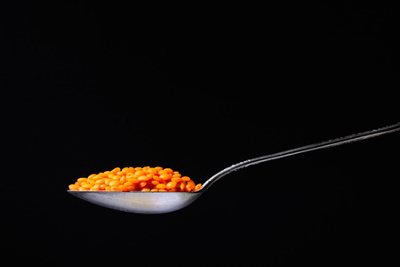 Metal silver spoon with the product in it. Orange lentils or beans. Large side view. Black dark background. Plenty of room for text.の写真素材