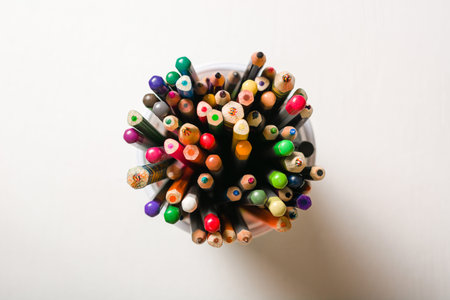 A lot of multi-colored pencils in a glass on a white background. View from above. School or art...