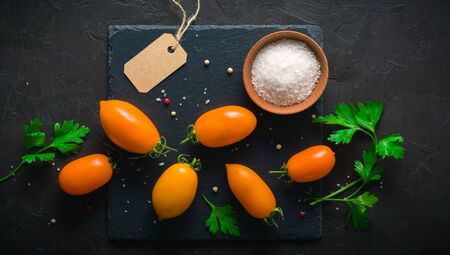 Fresh and juicy orange tomatoes laid out on a dark stone background. View from above. Place for textの写真素材