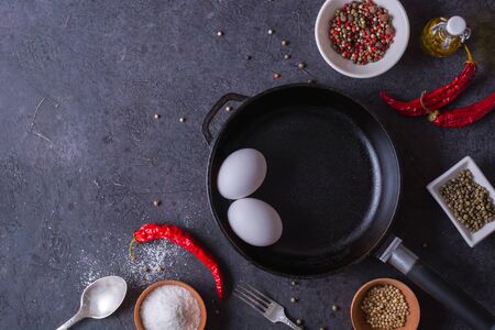Frying pan and eggs. Close up view of ingredients of fried egg and a frying pan. Empty cast iron pan, eggs, salt, pepper, oil and parsley on black background for cooking fried eggs.の写真素材