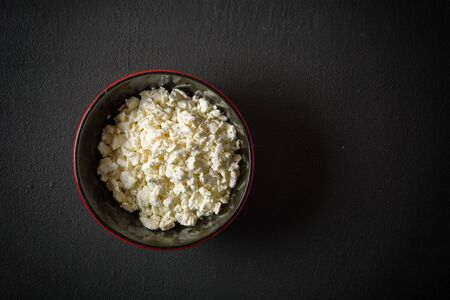 Fresh white cottage cheese in a bowl on the table. Tasty and healthy breakfast. dark stone surface. View from above. A lot of space for textの写真素材