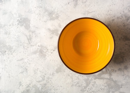 Empty yellow ceramic bowl on a light stone background.