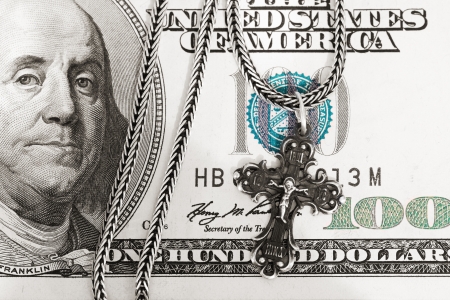 A hundred dollar bill with a silver cross on it meaning donationの写真素材