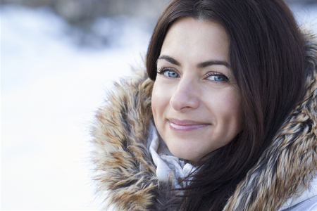 Portrait of a young pretty brunette woman wearing a jacket with fur collar outdoors in snowy January weather.の写真素材