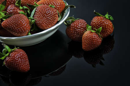 Fresh Strawberries in White Bowl on Black Plexiglassの写真素材
