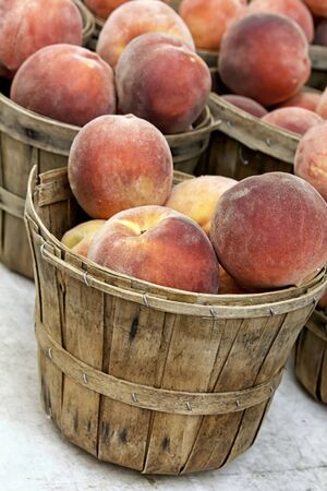Bushel baskets of fresh peaches on white table for sale at farmer s marketの写真素材