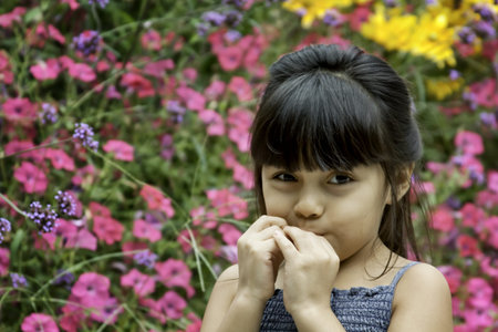 Little Girl Eating in Front of Flowers in Blue Dress