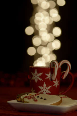 Red snowflake mug filled with warm drink with candy canes and snowman cookiesの写真素材