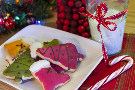 White plate full of colorful holiday cookies, with a candy cane and a glass of milk