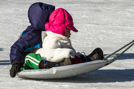 Parent pulling babies on snow saucer on outdoor skating rinkのeditorial素材