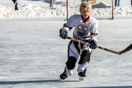 Young boy skating in hockey uniform with stick on outdoor hockey rinkのeditorial素材