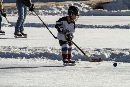 Boy in hockey gear, skating and hitting hockey puck on outdoor skating rinkのeditorial素材
