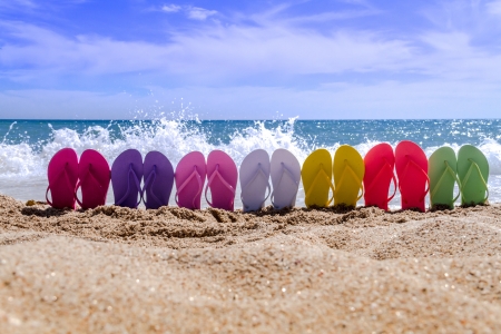 Line of brightly colored flip flops arranged in a rainbow on beach with large waves breaking on sandy shoreの写真素材