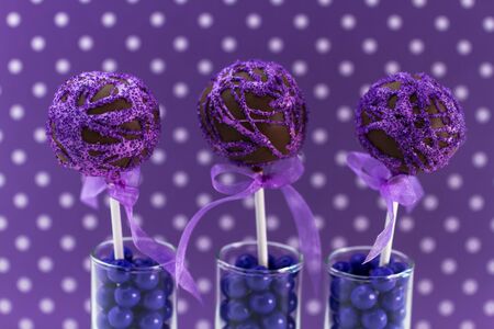 Purple swirled chocolate cake pops with purple polka dot background standing in candy filled shot glassesの写真素材