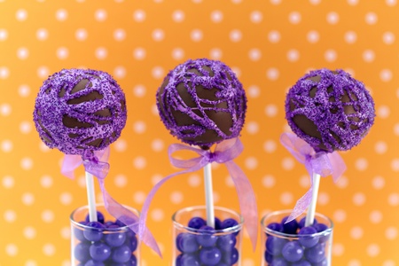 Purple swirled chocolate cake pops with orange polka dot background standing in candy filled shot glassesの写真素材